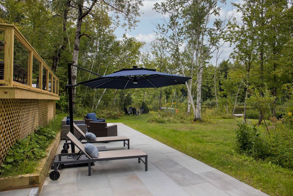 Lounge chairs with navy patio umbrella on stone patio beside wooden deck and garden.