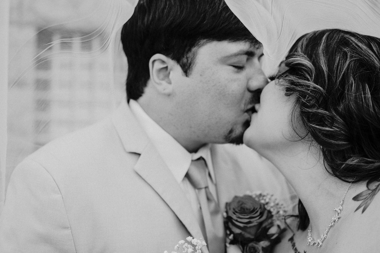 Black and white photo of a couple sharing a romantic kiss at their wedding ceremony.