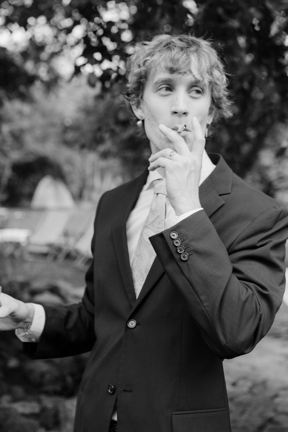 Elegant man in black suit smoking cigarette outdoors in black and white portrait photography.