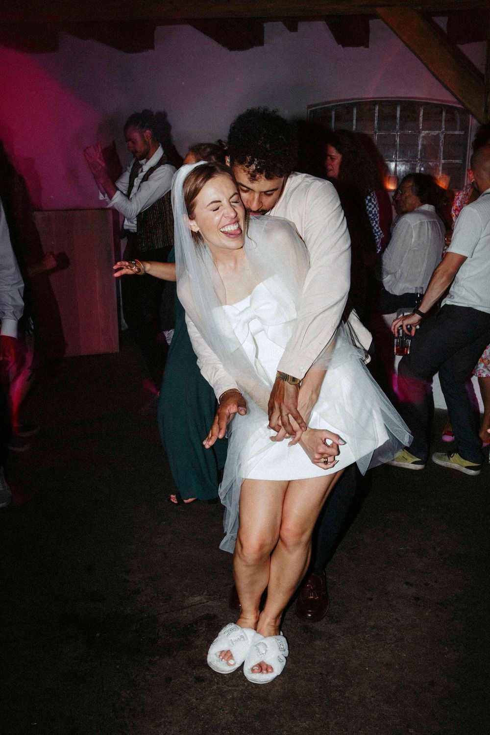 Bride in white dress and veil dances joyfully with groom at wedding reception party.