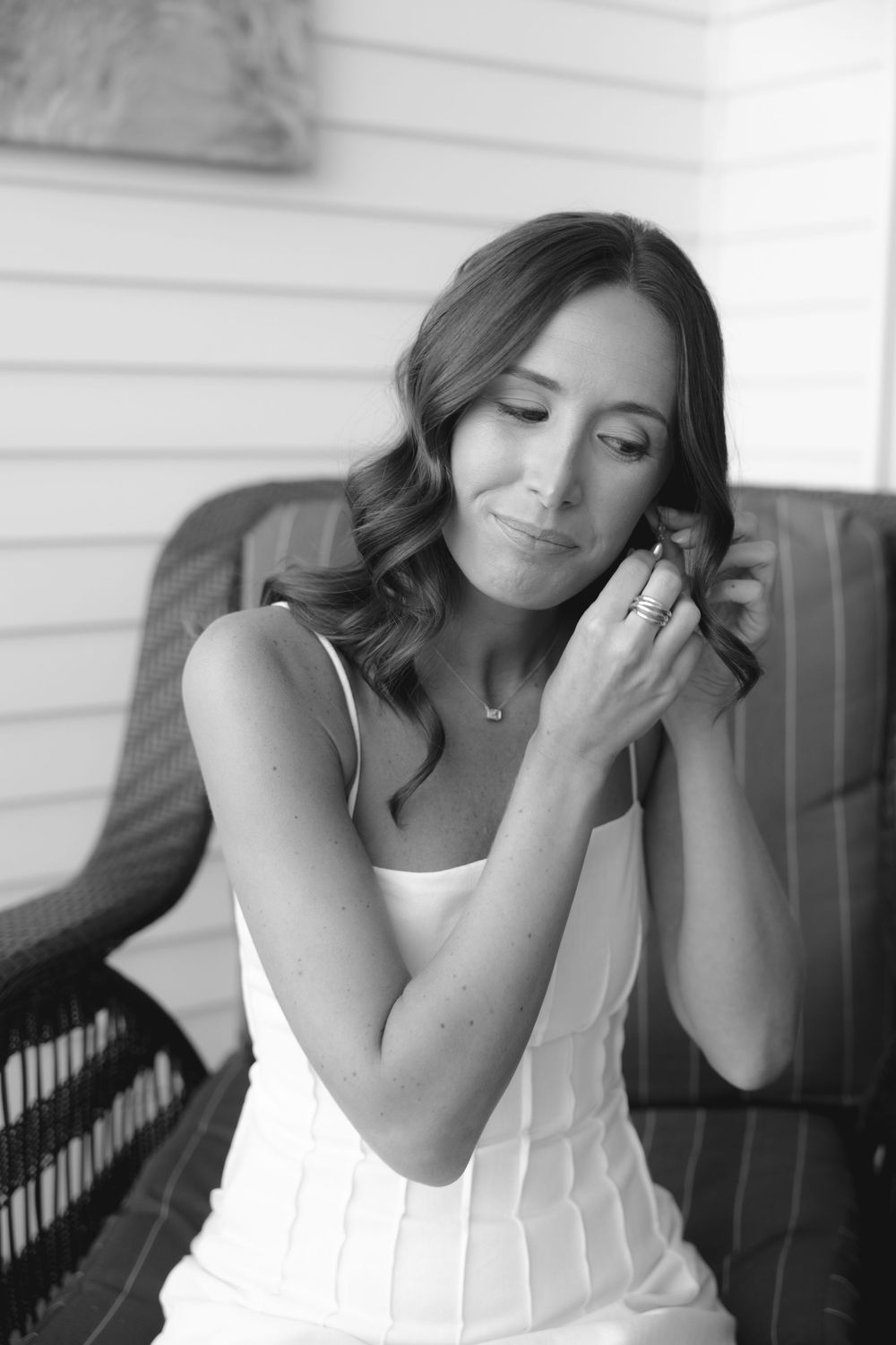 Black and white portrait of bride putting on earrings in white dress before wedding.