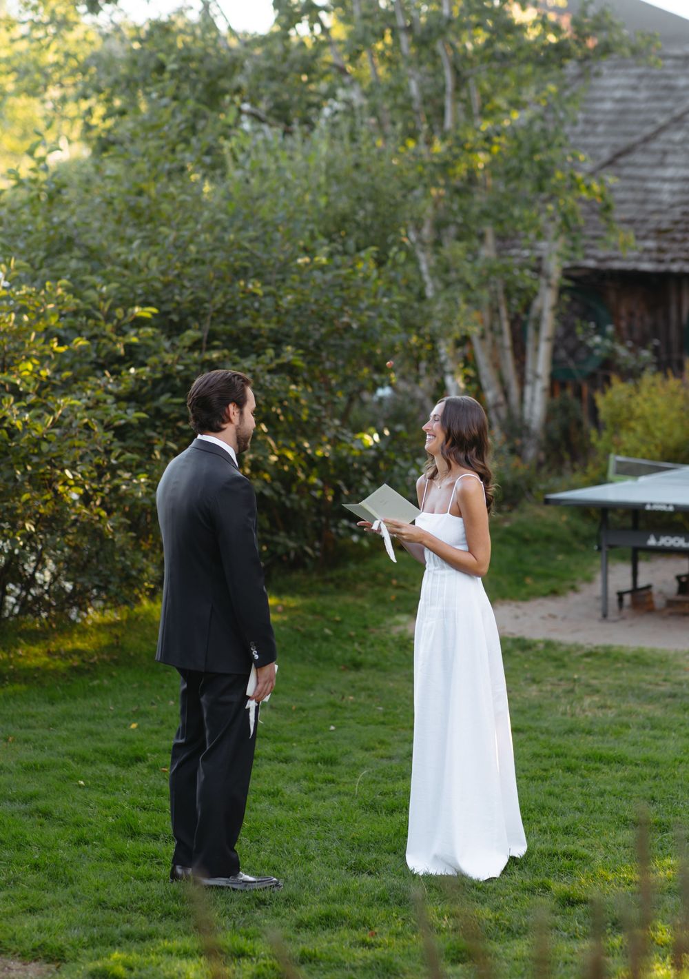 Bride reads vows to groom during outdoor garden wedding ceremony at golden hour.