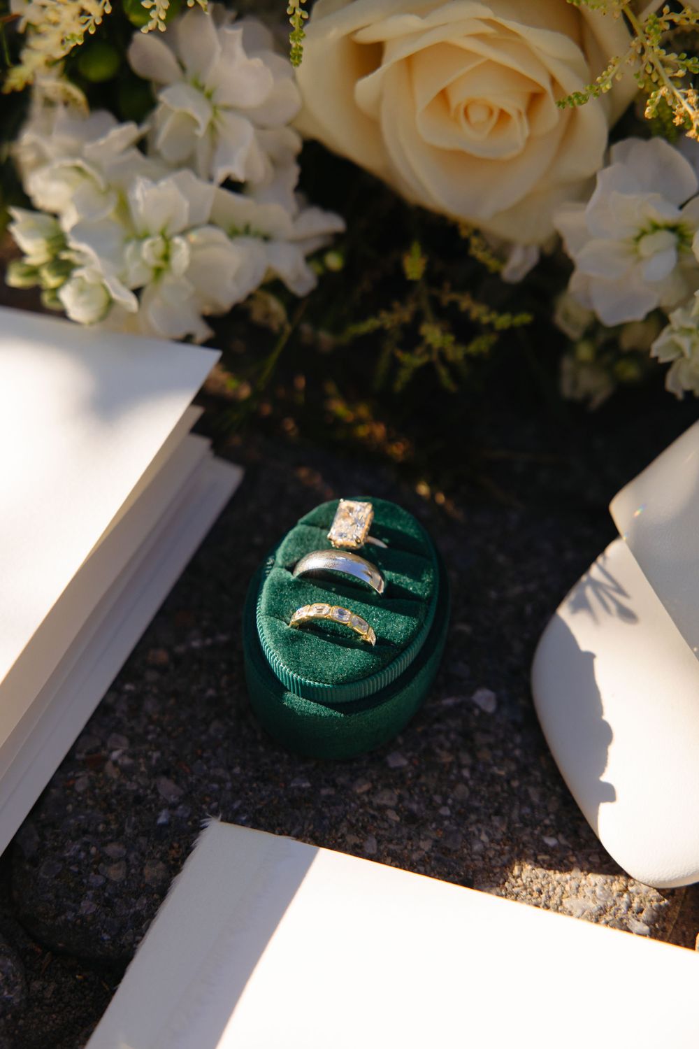 Three wedding rings displayed in a green velvet ring box beside a white rose bridal bouquet.