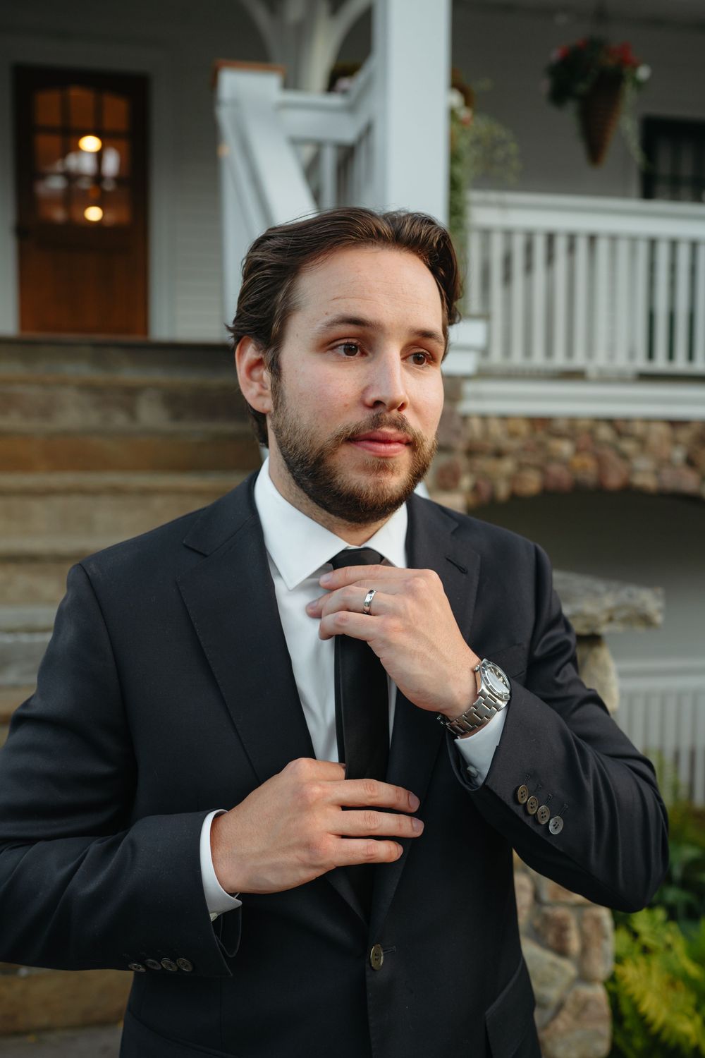 Groom in dark suit adjusting tie outdoors before wedding ceremony at Mirror Lake Inn.