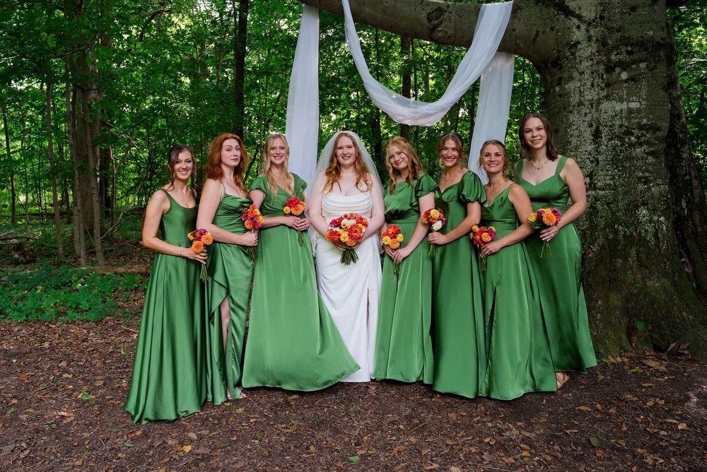 Bridesmaids in kelly green dresses hold colorful wildflower bouquets in a lush Michigan forest wedding setting.