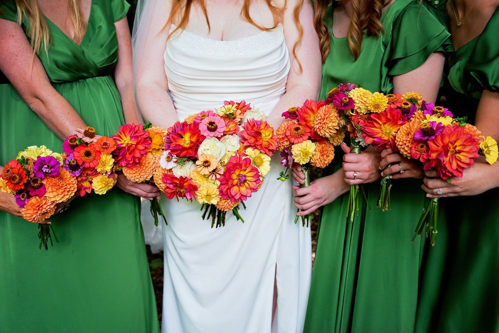 Close-up of bridesmaids in green satin dresses hold colorful wildflower bouquets in a lush Michigan forest wedding setting.