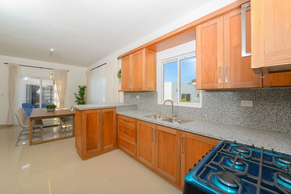 Modern kitchen with wooden cabinets, granite backsplash, gas stove, and open dining area view.