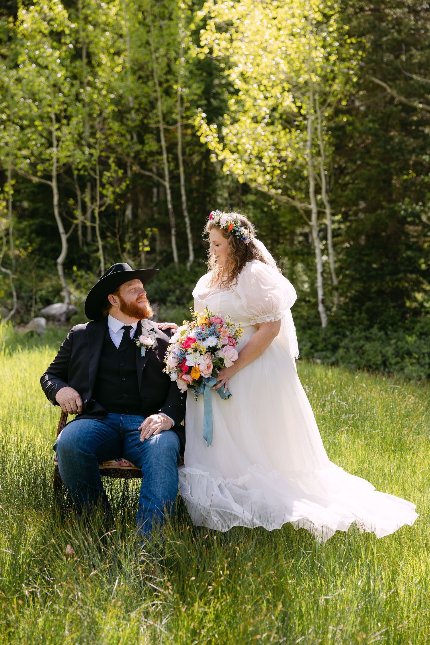 Bride and groom share a joyful moment outdoors, she in a beaded gown with veil, he in a dark suit with blue tie.