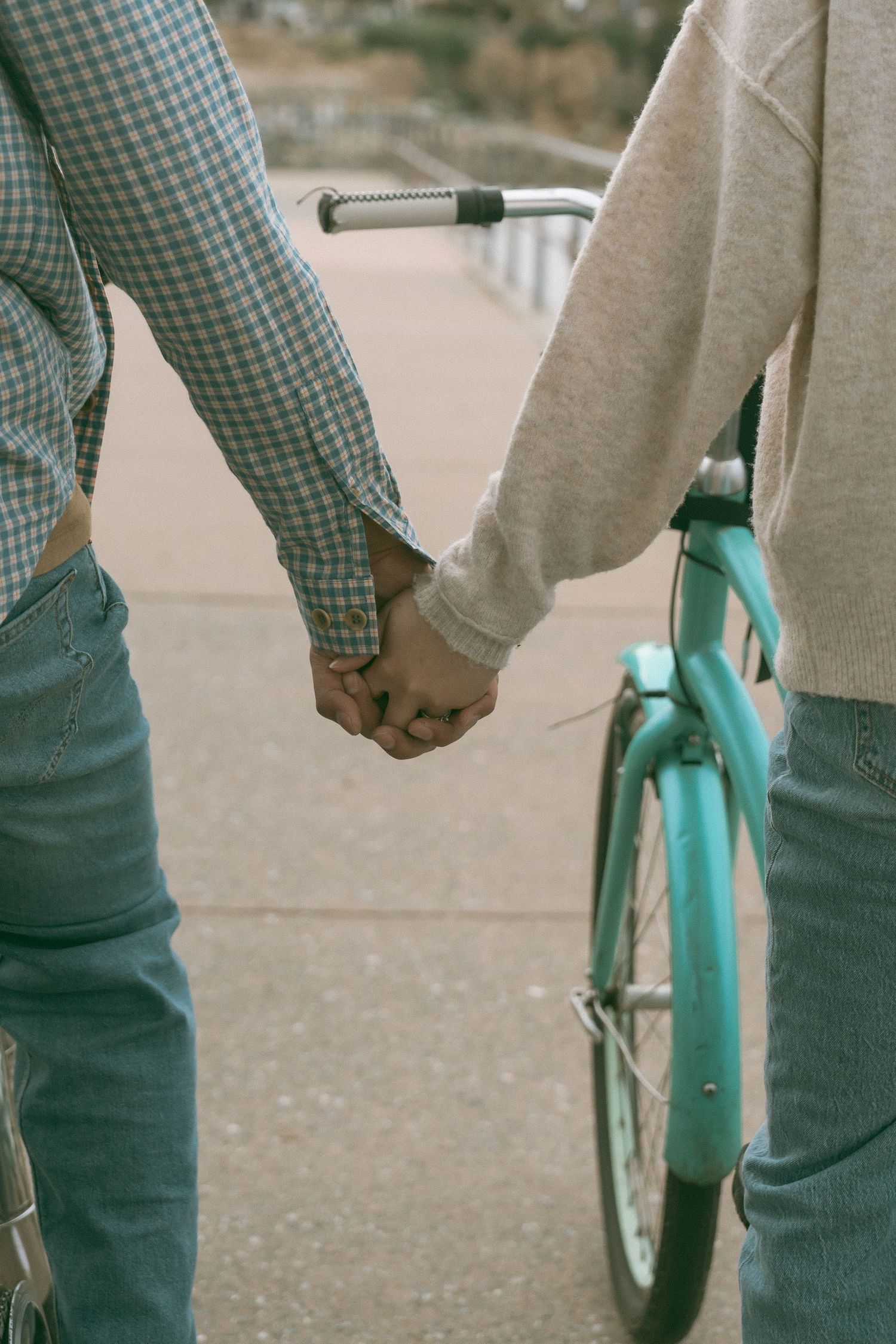 Couple holding hands next to a teal bicycle on a paved path, wearing jeans and casual tops.