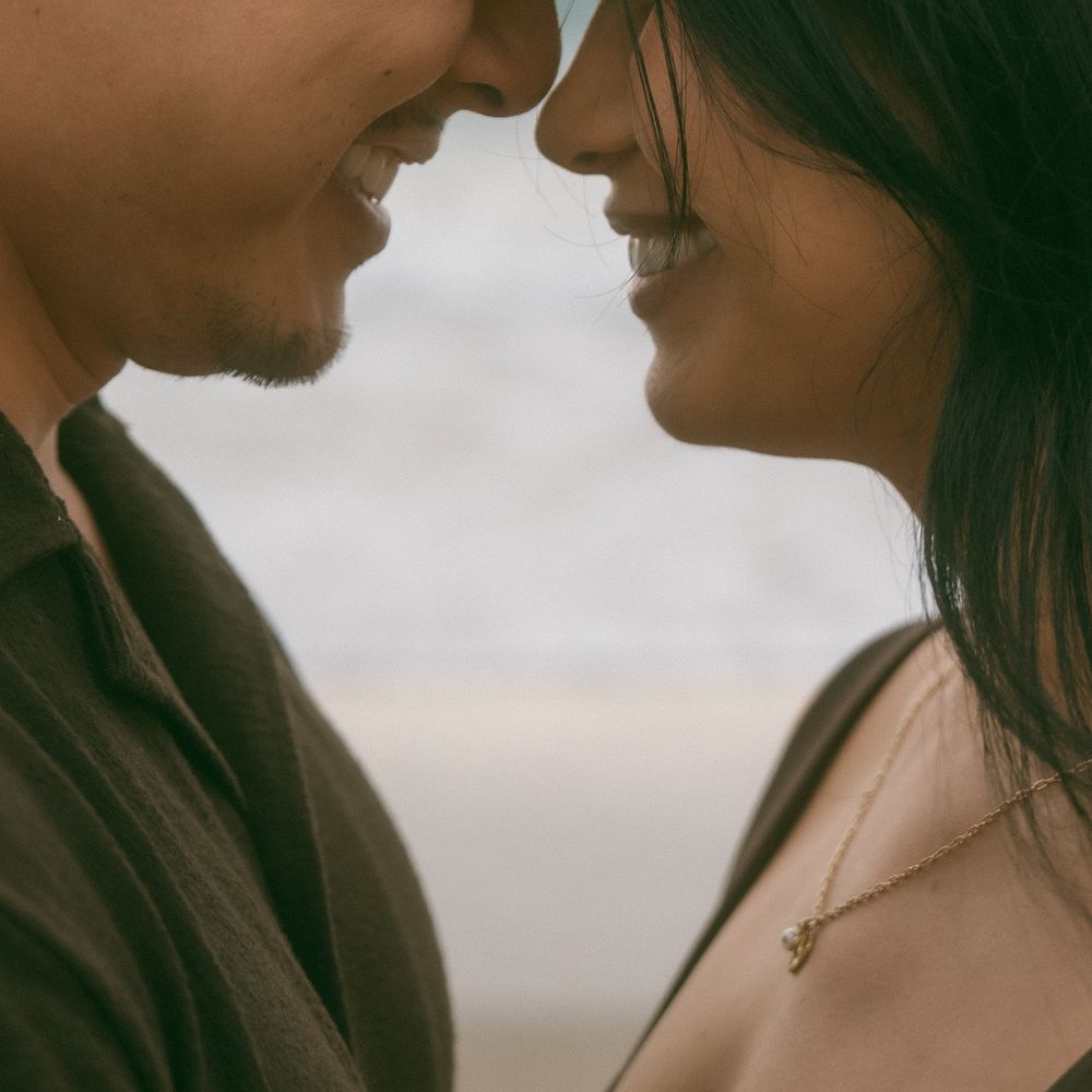 A couple sharing a romantic moment, faces close together, smiling softly outdoors on a cloudy day.