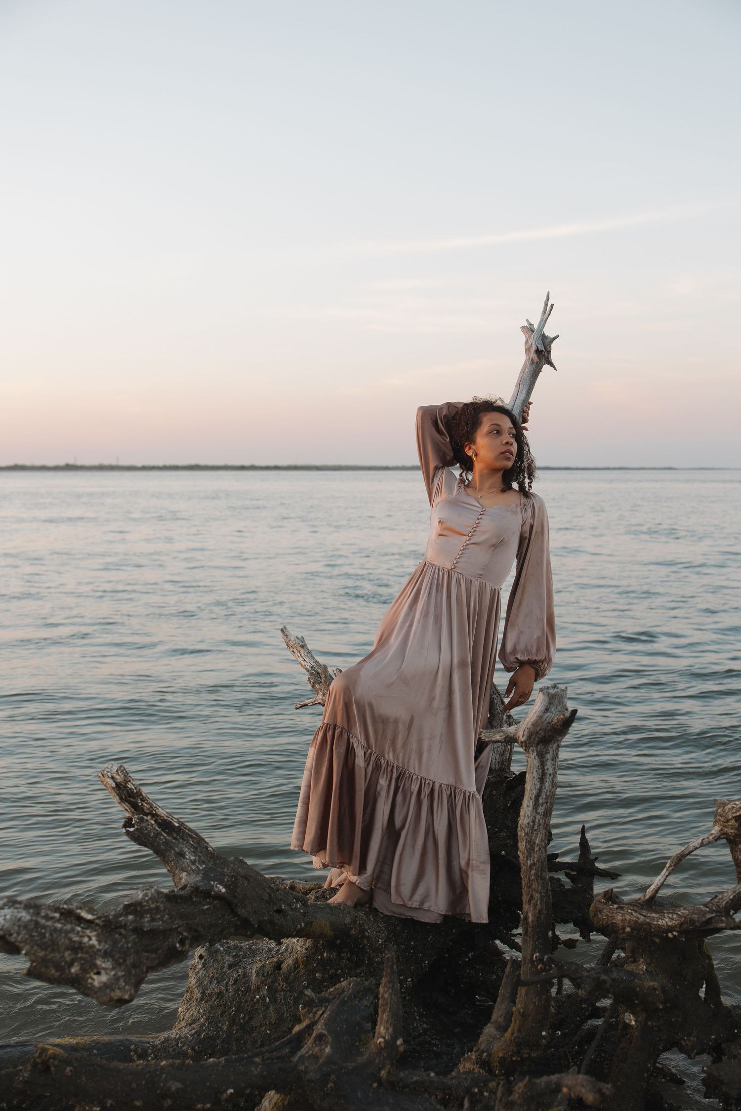 A woman at sunset leaning against driftwood