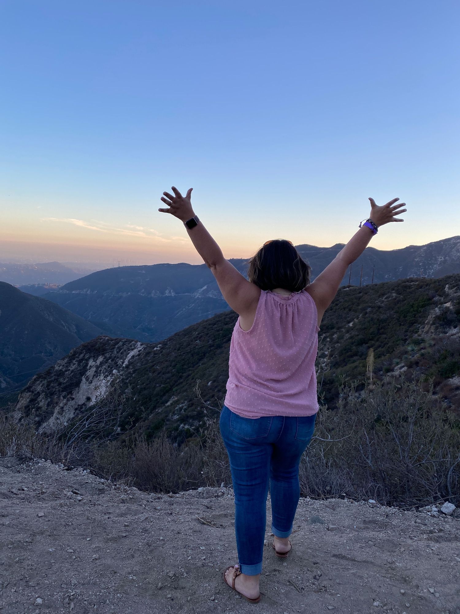 Woman with arms raised celebrating mountain canyon sunset view from hiking trail overlook.