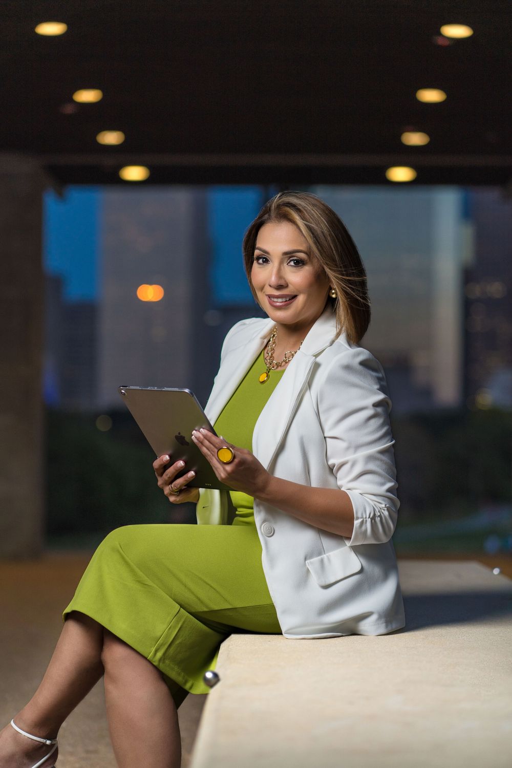 Business professional in white blazer and lime dress works on tablet.