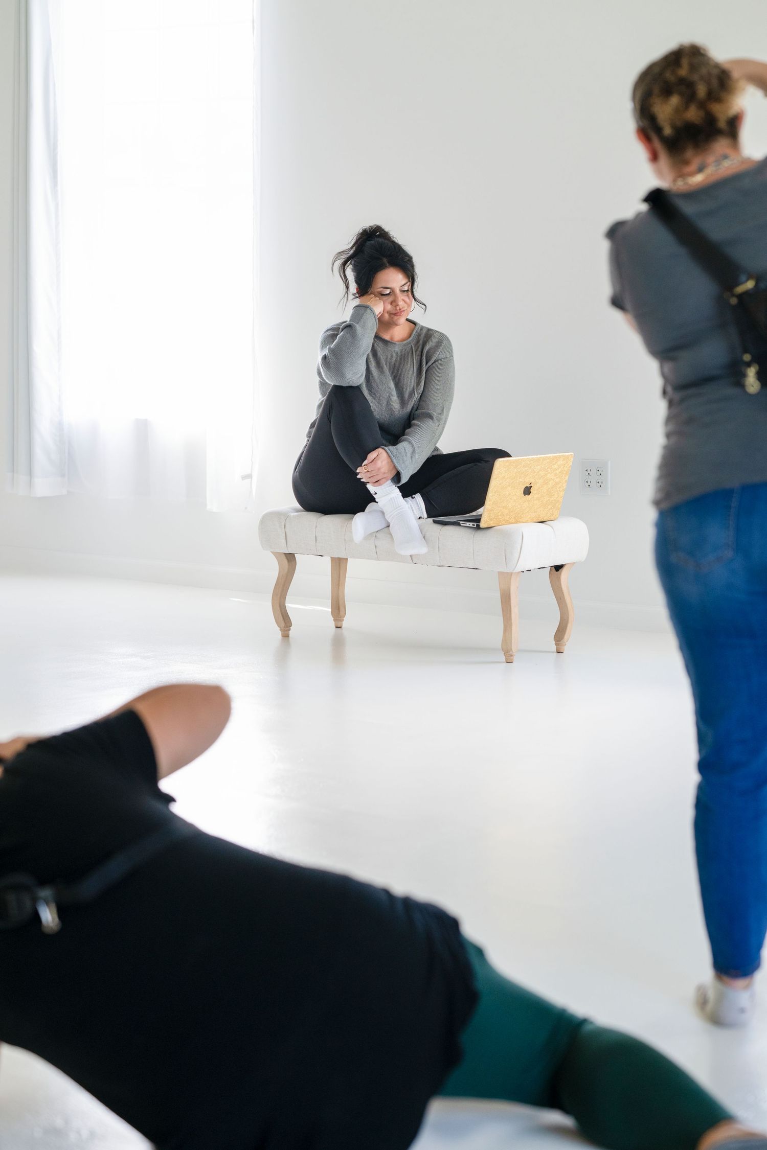 Woman sitting on a bench with a laptop during a professional photo shoot in a bright white studio.