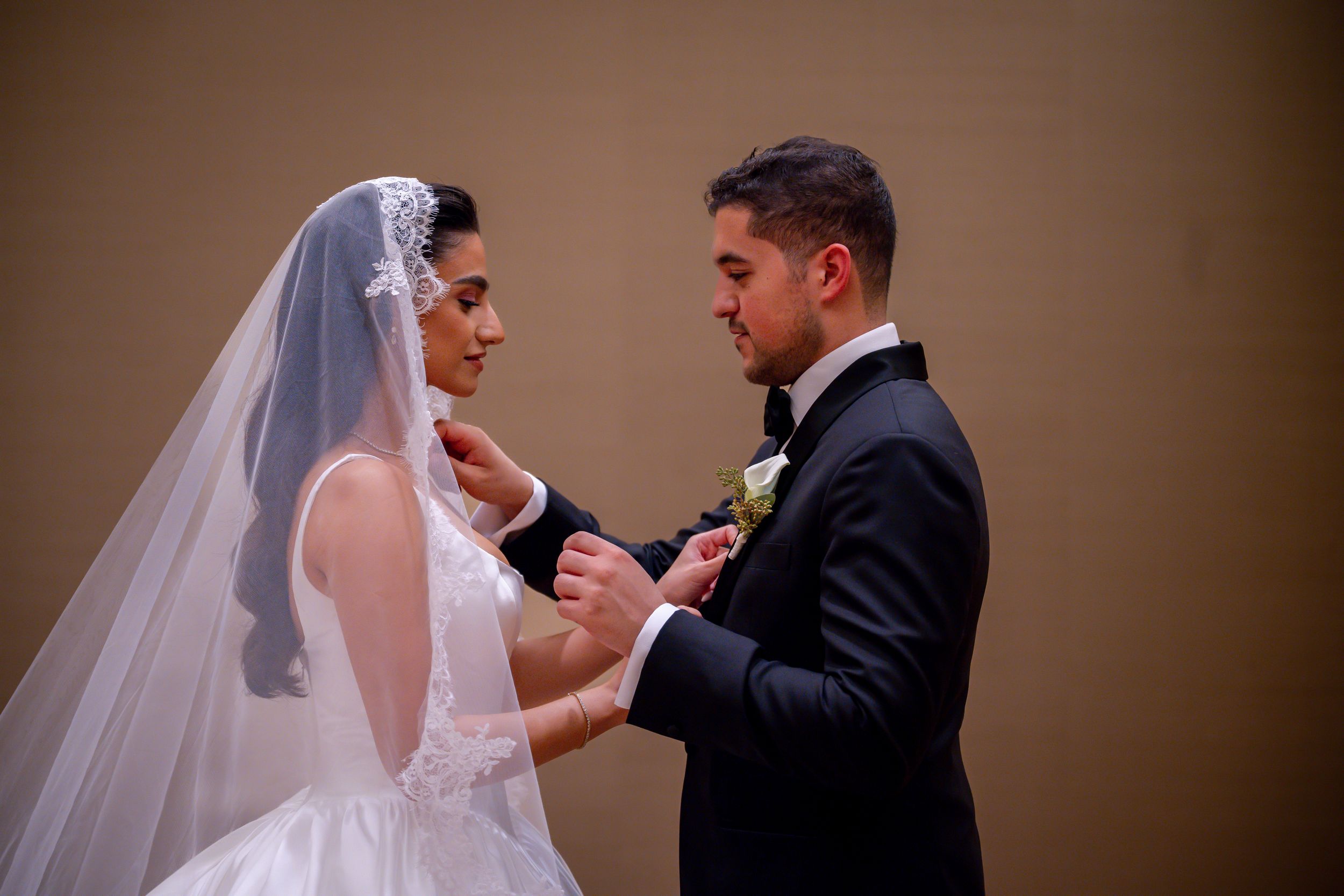 Bride and groom exchanging rings during wedding ceremony, bride wearing white gown and veil, groom in black tuxedo.