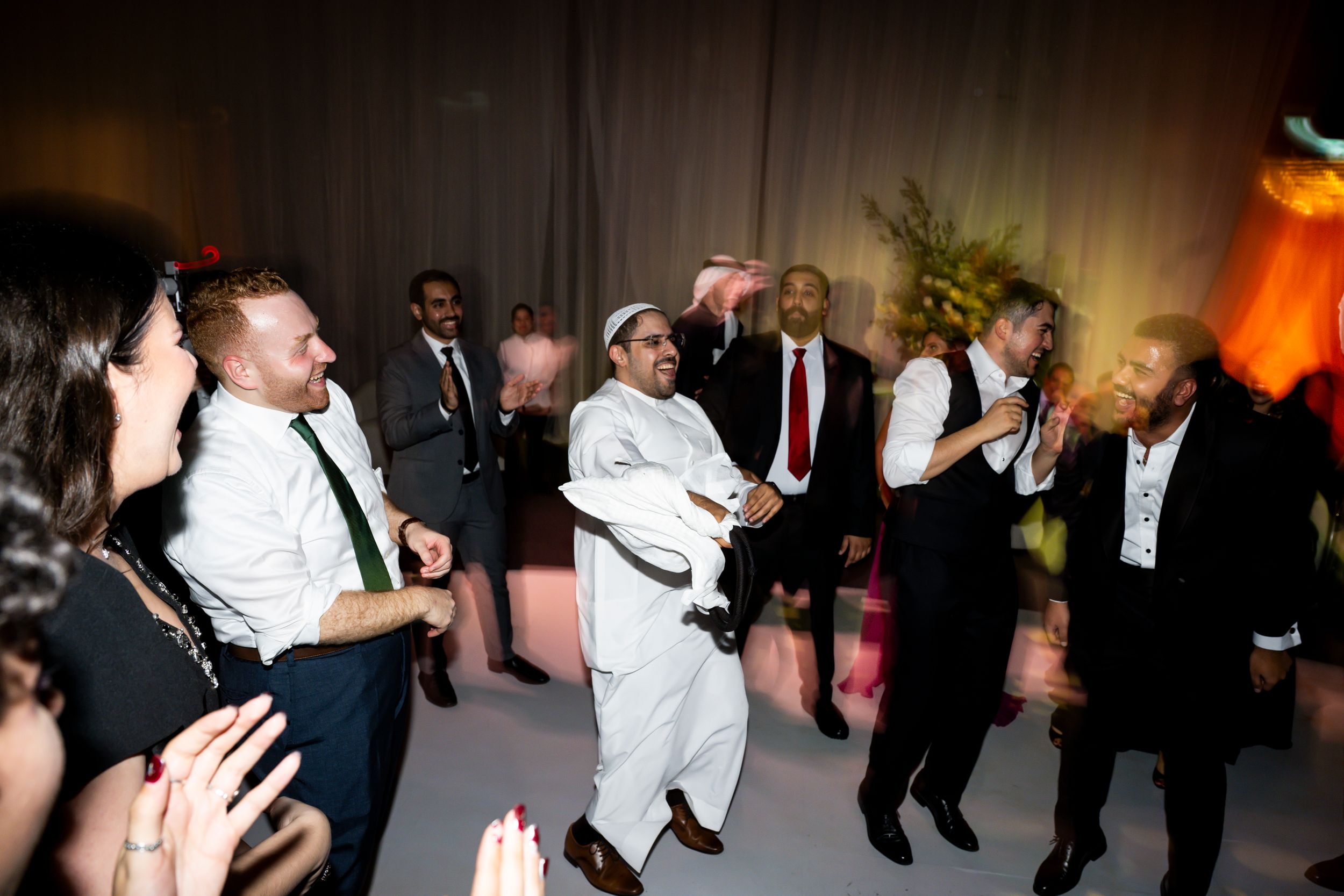 Guests dancing and celebrating at a lively wedding reception party in formal attire.