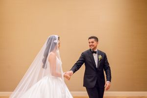 Bride and groom holding hands smiling at each other in elegant wedding attire.
