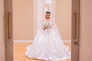Elegant bride in a white ball gown wedding dress holding a floral bouquet in a grand hallway.