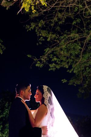 Bride and groom share a romantic moment under a tree at night, illuminated by a soft spotlight.