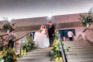 Bride and groom descend floral-decorated staircase at elegant indoor wedding ceremony venue.