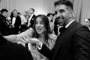 Black and white photo of a joyful couple at a formal wedding reception, laughing and reaching toward the camera.