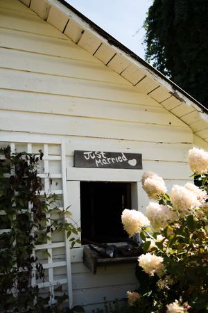 White wooden barn with a chalkboard Just Married sign above a window, surrounded by blooming white hydrangeas.