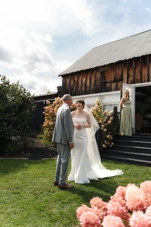 Bride and groom sharing an intimate moment on a green lawn outside a rustic wooden barn wedding venue.