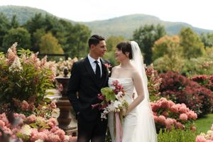 Bride and groom stand among pink hydrangeas with mountain views on their wedding day.
