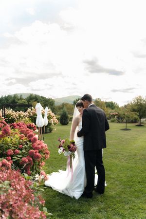 Bride and groom stand among blooming red flowers in a lush garden with mountain views on their wedding day.