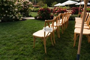 Rows of wooden crossback chairs set up on green lawn for outdoor wedding ceremony beside blooming hydrangea bushes.