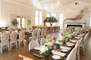 Elegant wedding reception hall with long wooden tables, floral centerpieces, chandelier, fireplace, and lush greenery decor.