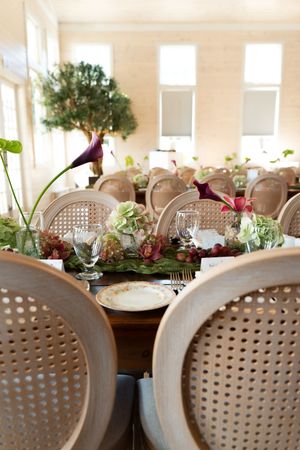 Elegant wedding reception table with calla lilies, hydrangeas, cane chairs in a bright venue.