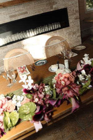 Wedding sweetheart table adorned with pink and burgundy floral arrangements near a modern fireplace.