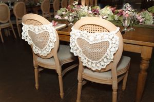 Elegant wooden wedding chairs adorned with white lace heart-shaped decorations at a reception table.