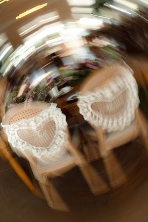 Blurred artistic shot of two wedding chairs with lace heart decorations at a romantic reception venue.