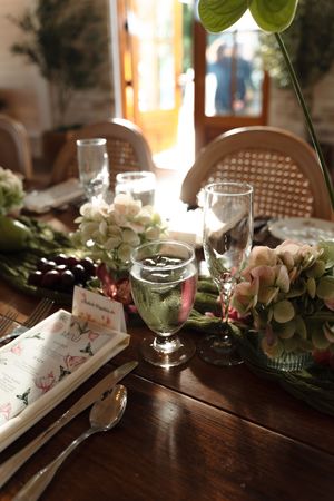Romantic wedding reception table with crystal glassware, white hydrangeas, and floral menu cards in warm light.