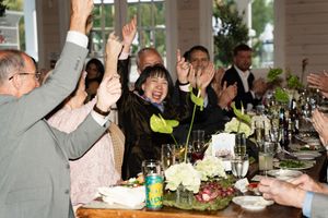 Joyful wedding guests raising hands and clapping at a floral-decorated reception dinner table.