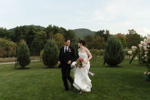 Bride and groom walk hand in hand across lush green lawn with mountain backdrop at outdoor wedding ceremony.