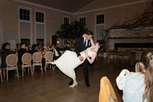 Groom dipping bride during first dance in an elegant white ballroom surrounded by wedding guests.