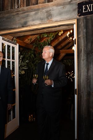 Elegantly dressed wedding guest holding champagne while entering a rustic barn venue with string lights.