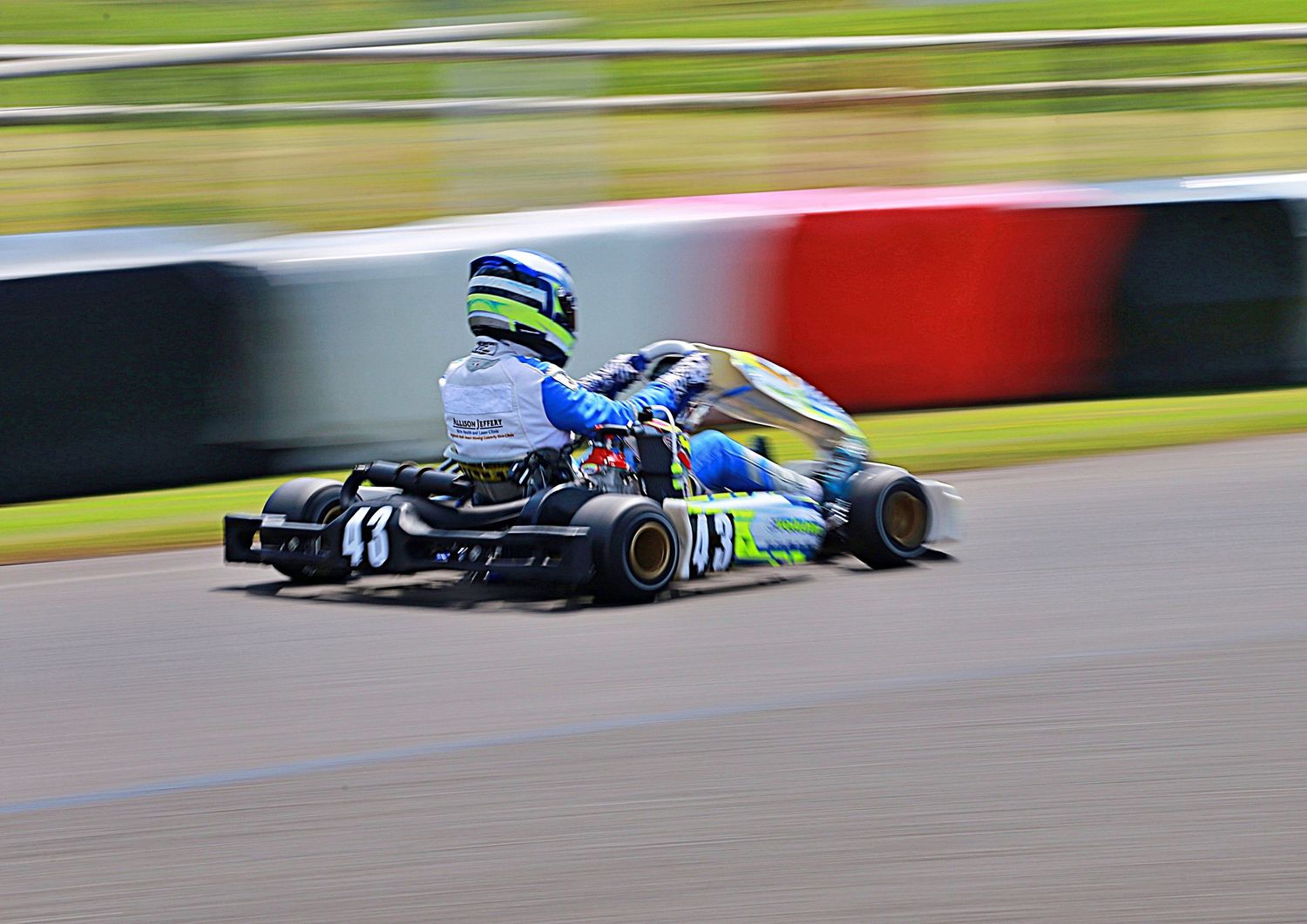 Blue and white go-kart racing at speed on a circuit with motion blur effect.