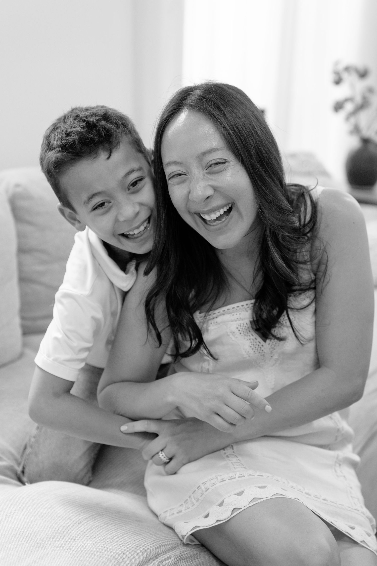 A laughing woman and boy share a joyful hug on a sofa in black and white.