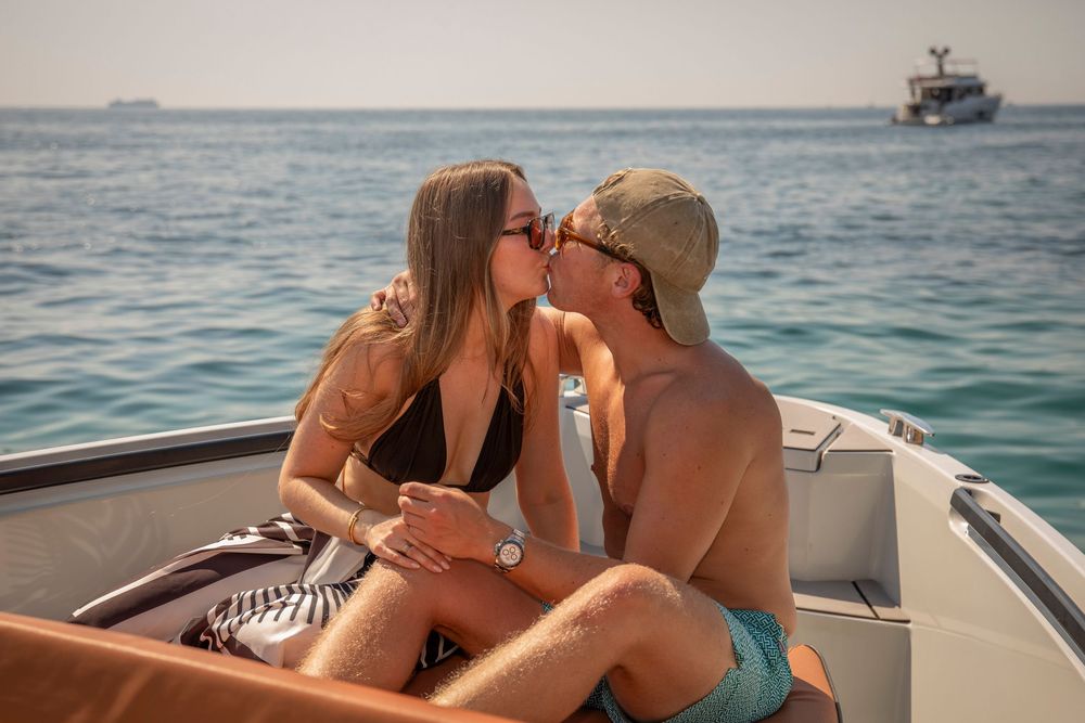 Side profile of a couple kissing on the bow of a boat out at sea, with another small vessel visible on the horizon.
