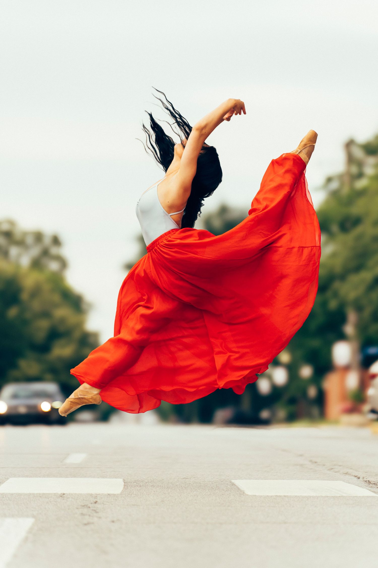 Professional dancer leaps in the air across a Crown Point crosswalk, senior portrait photographer, hair and skirt in motion.