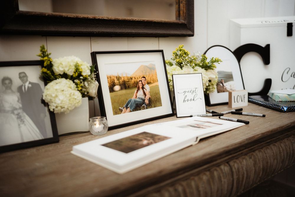 Wedding guest book table with framed engagement photos, white hydrangeas, and decorative signage display.
