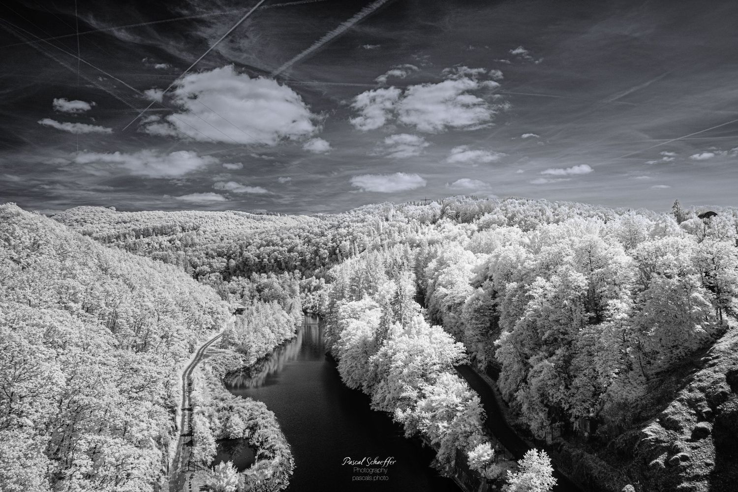 Aerial infrared black and white photo of a winding river through dense forest under dramatic cloudy sky.