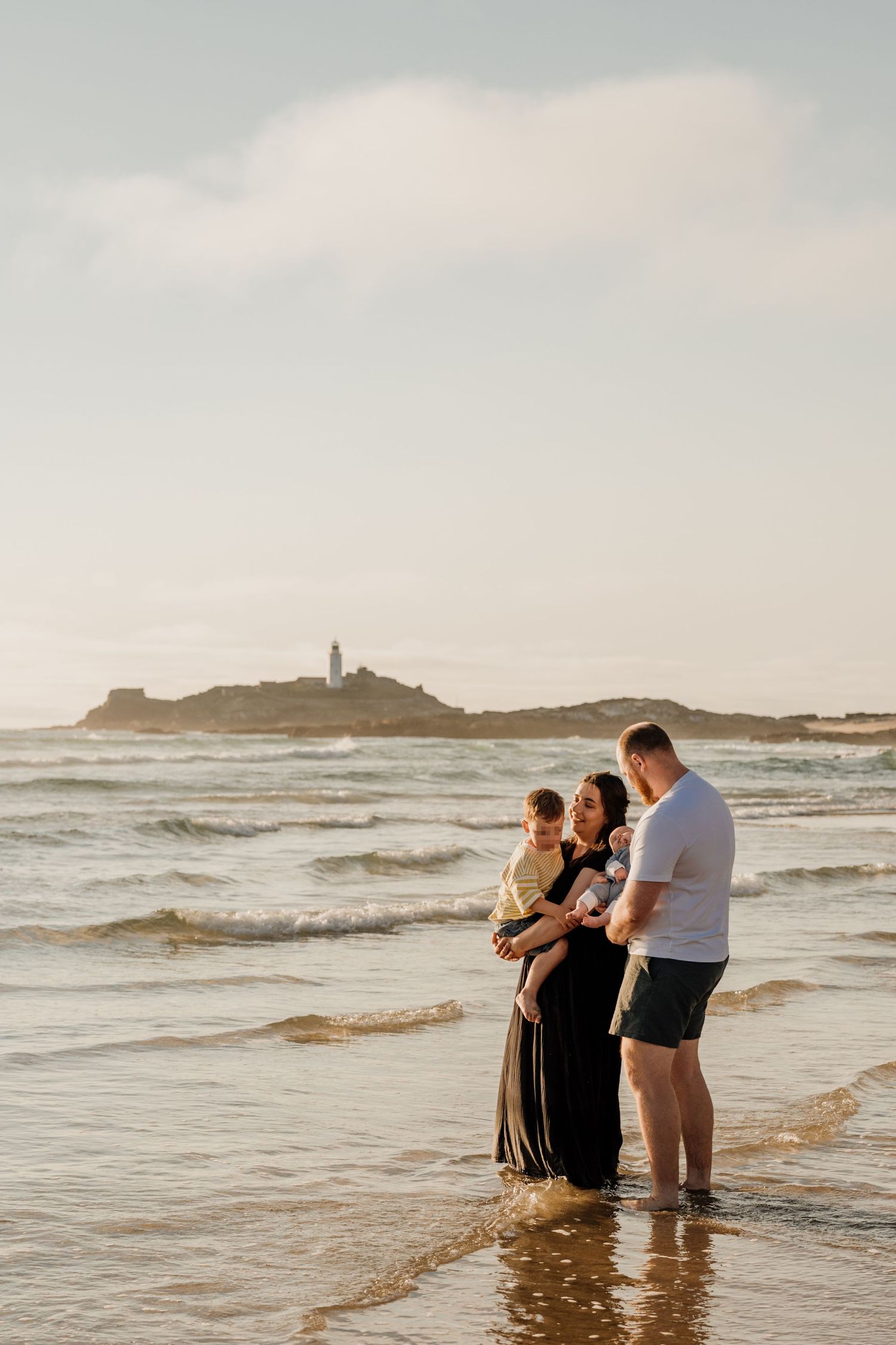 Family of four standing in ocean waves at golden hour, on Godrevy Beach during family photoshoot by ryan goold photography