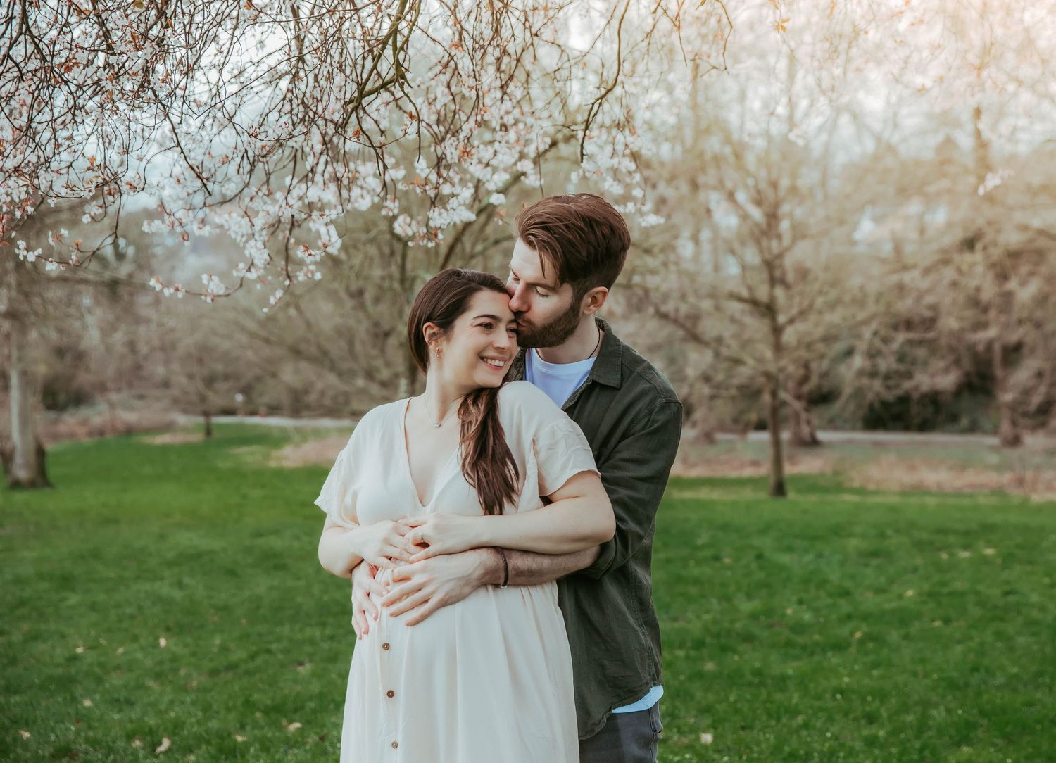 Couple embracing romantically under blooming spring trees in a lush green park during a maternity session in south east London