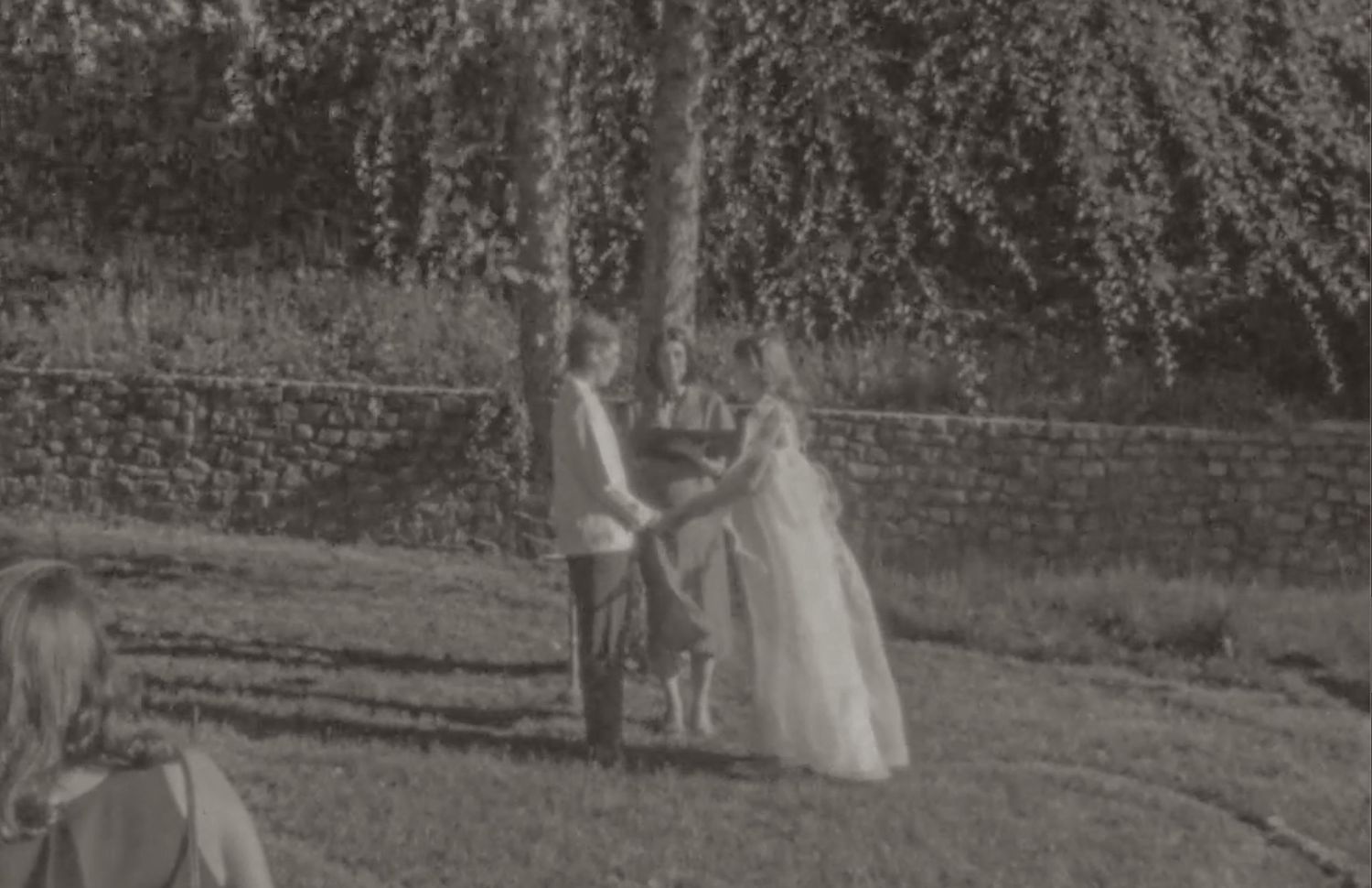 Black and white photo of a couple sharing a romantic moment outdoors on their wedding day, surrounded by lush trees.