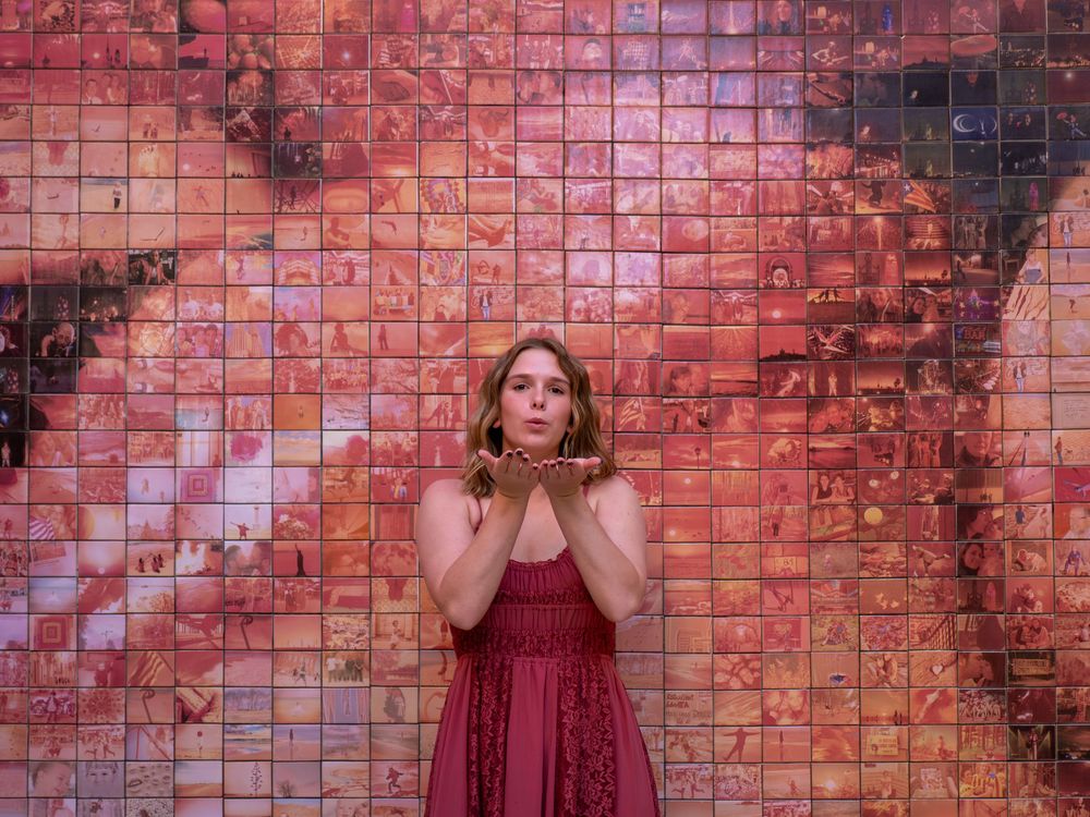 Woman in red dress blowing glitter in front of a colorful mosaic tile wall mural.